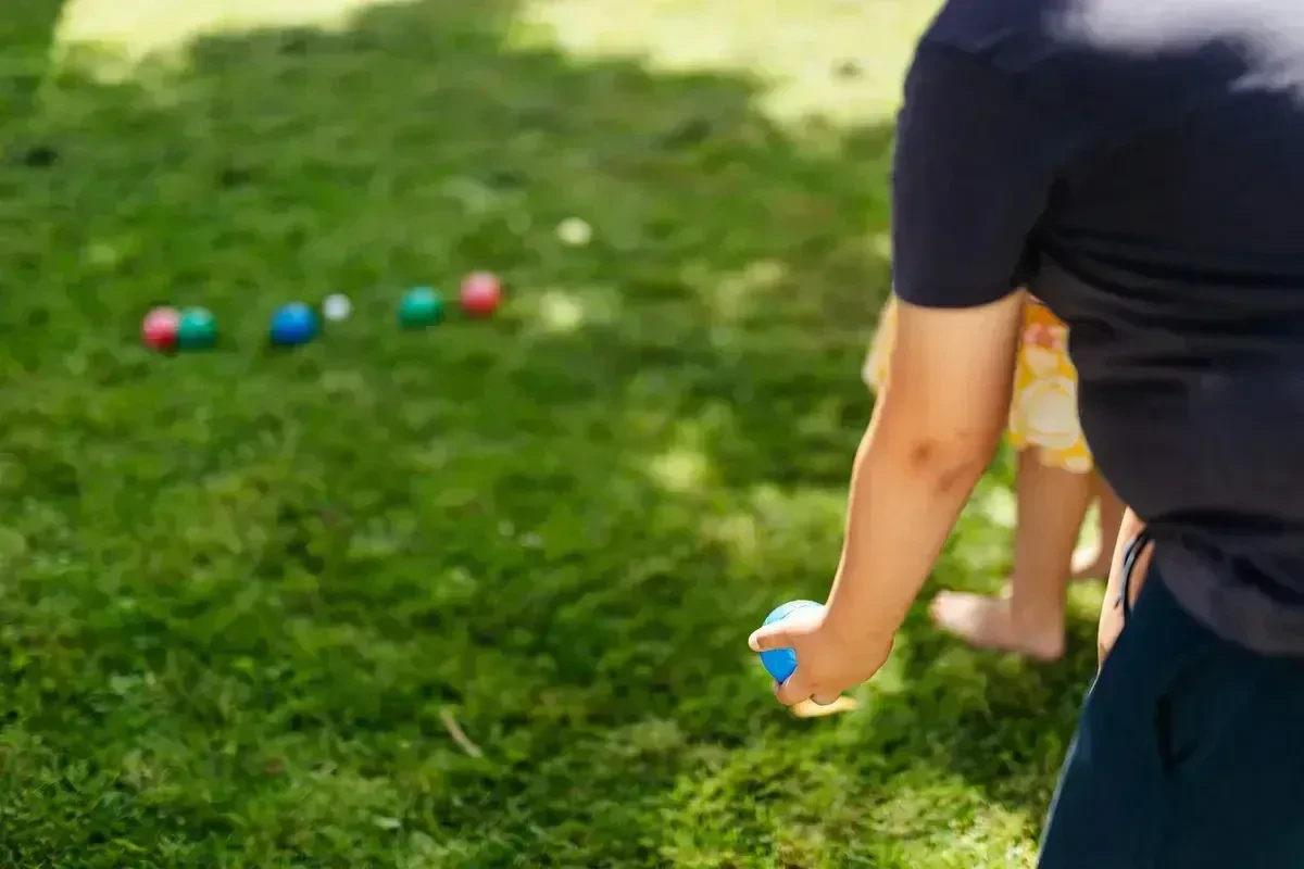 Father and daughter playing bocce ball together on a sunny backyard lawn