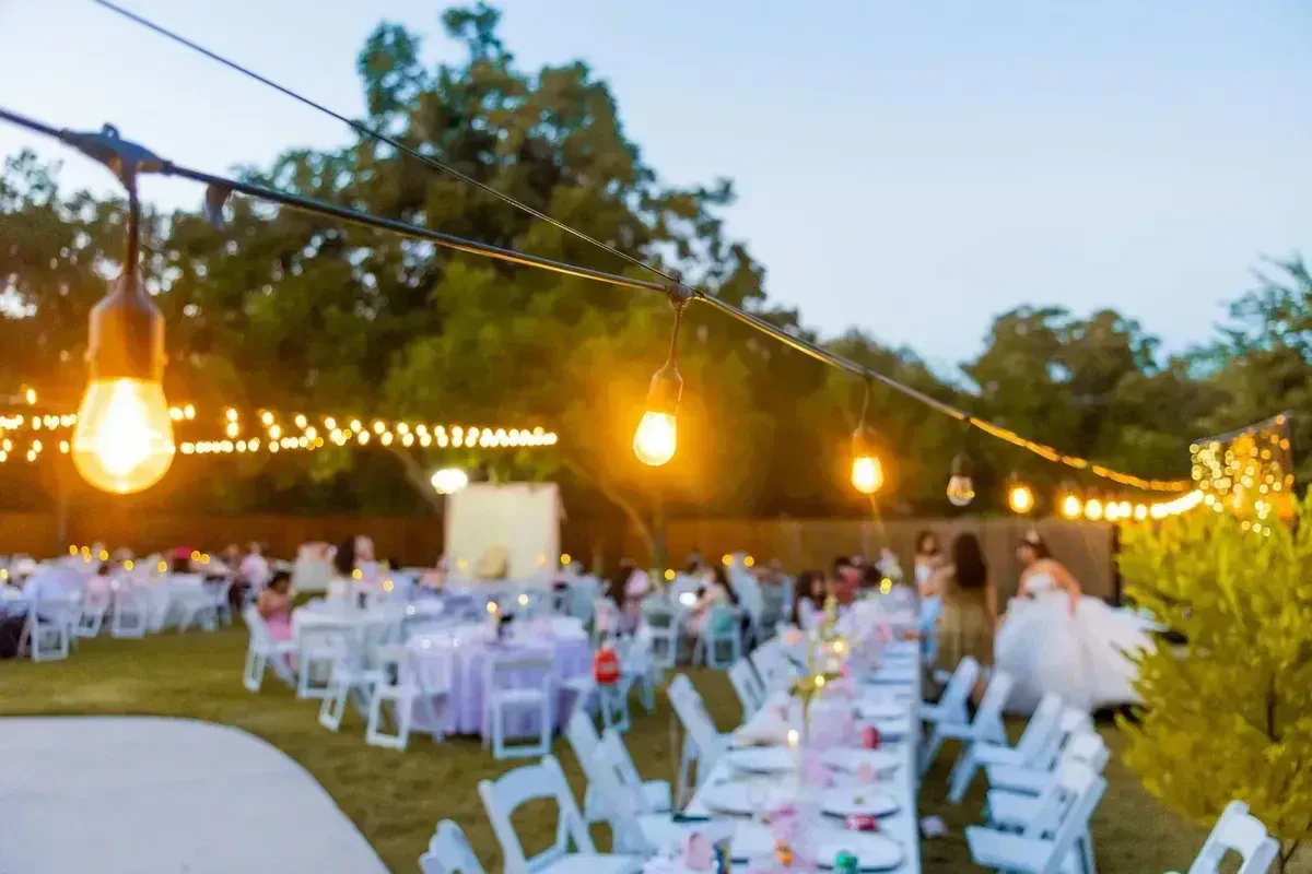 Outdoor wedding reception on a lawn at sunset with string lights glowing over the tables